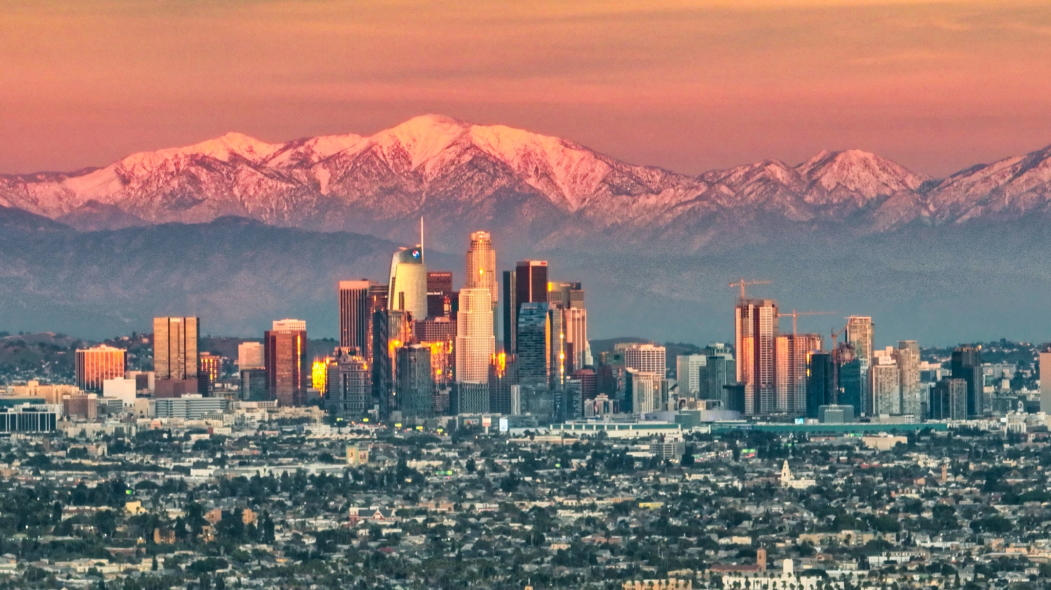 Downtown Los Angeles at sunset with snow-covered mountains behind the skyline