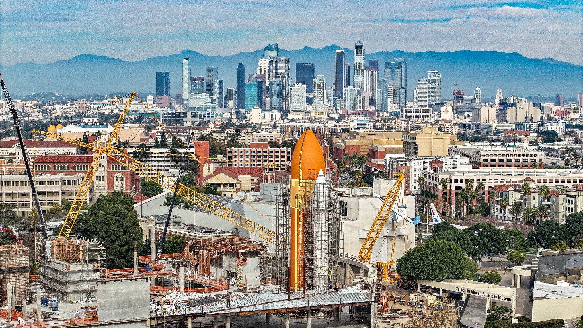 Space Shuttle Endeavour construction site with cranes and downtown Los Angeles behind it