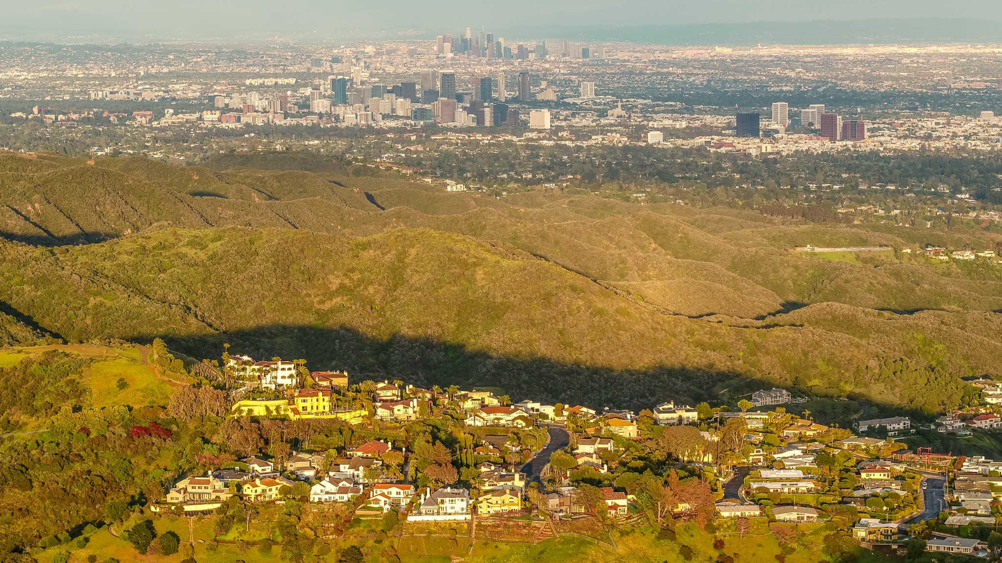 Golden-hour aerial view over hillside homes toward West Los Angeles and downtown