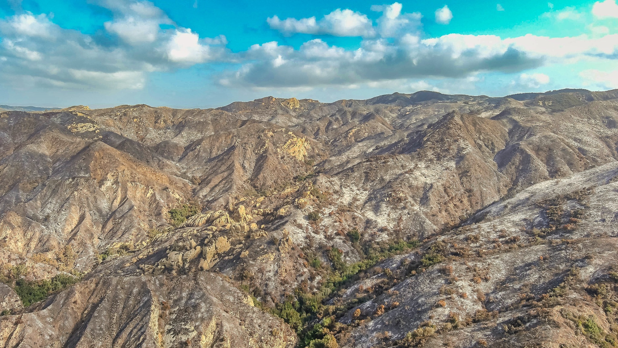 Aerial panorama of fire-affected mountain ridges under a blue sky